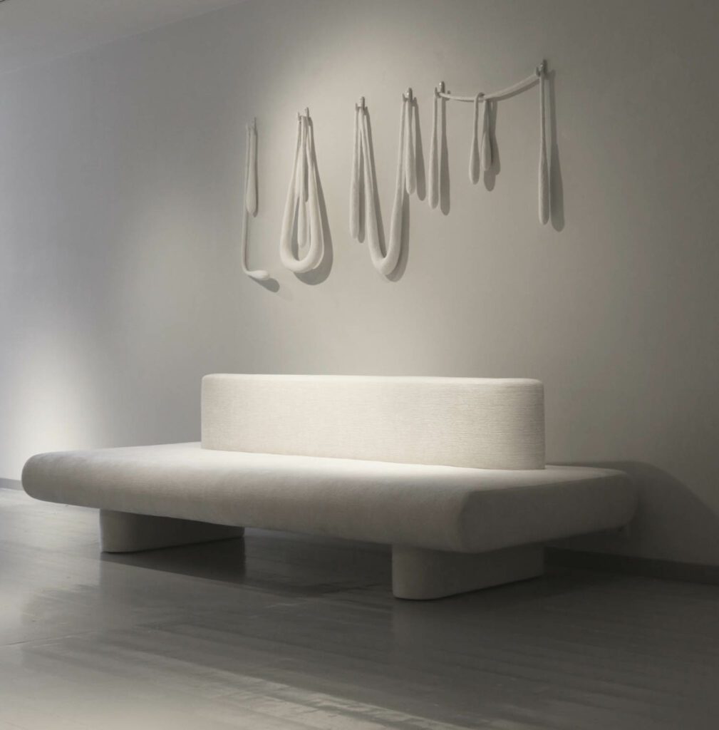 A minimalist white bench and hanging sculpture above it. 