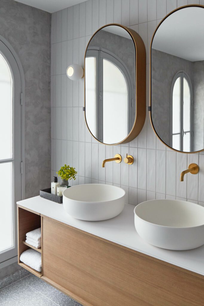 The primary bathroom comes to life with sinks by Inbani, Hotbath faucets, cabinets by Tailormade Stocco, wall sconces by Faro Barcelona, Ressources Peintures paint, and