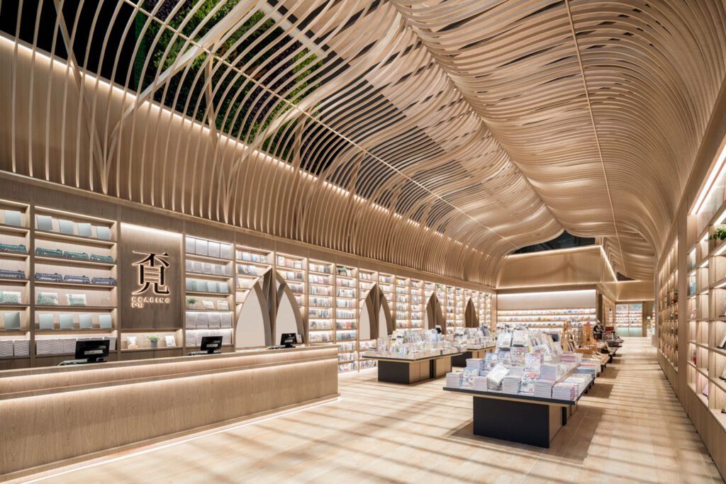 The double-height entrance hall of Reading Mi, a bookstore in Foshan, China, has a herringbone ceiling of timber-print aluminum slats that takes the form of an open book.
