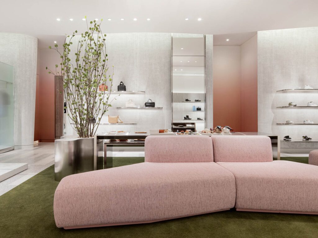 A pink couch on a green rug offers guests a space to try on shoes. 