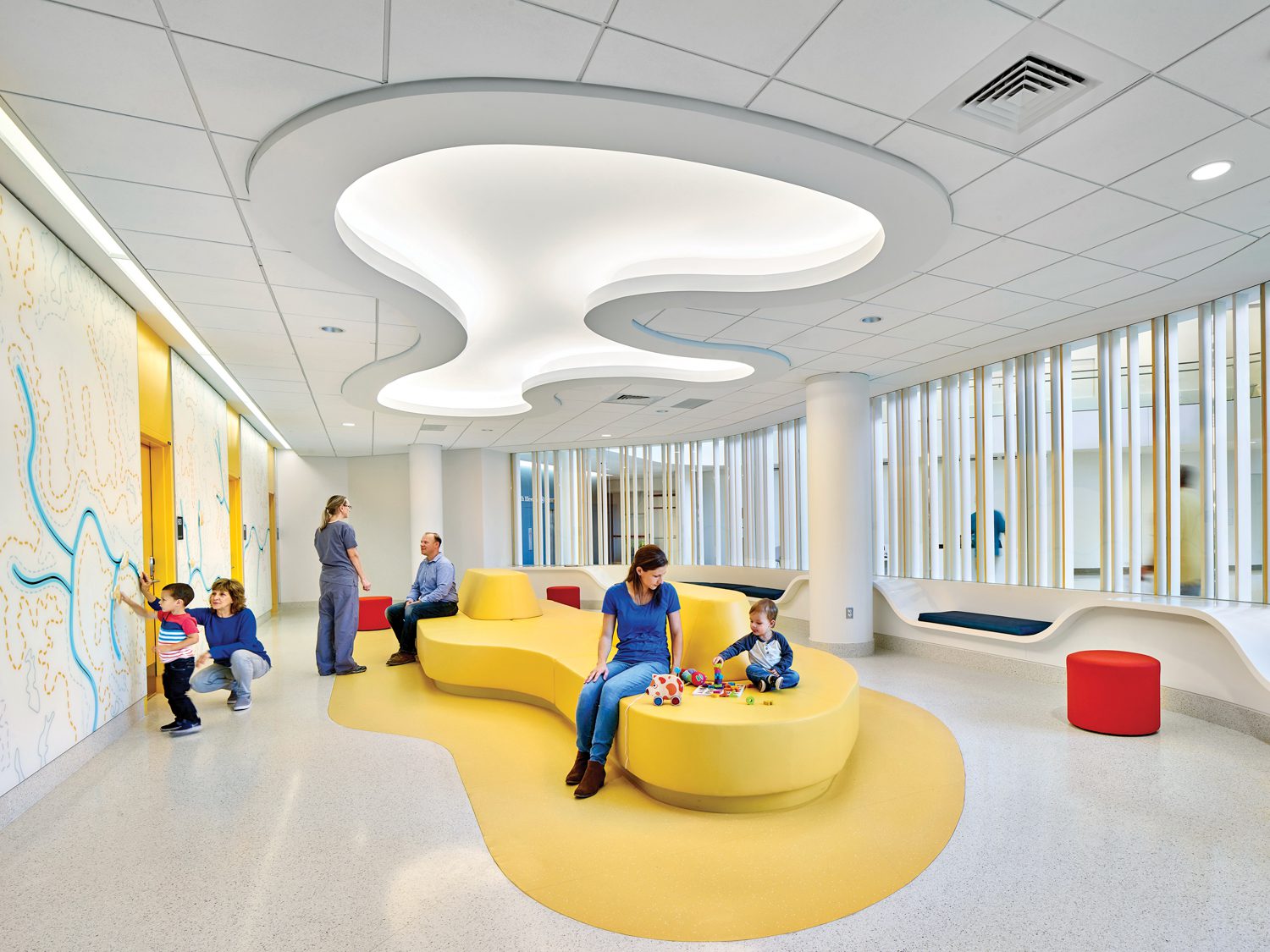 Yellow curved couch beneath a similarly shaped illuminated pattern on the ceiling above in University of Virginia hospital expansion, Charlottesville, by Perkins&Will.