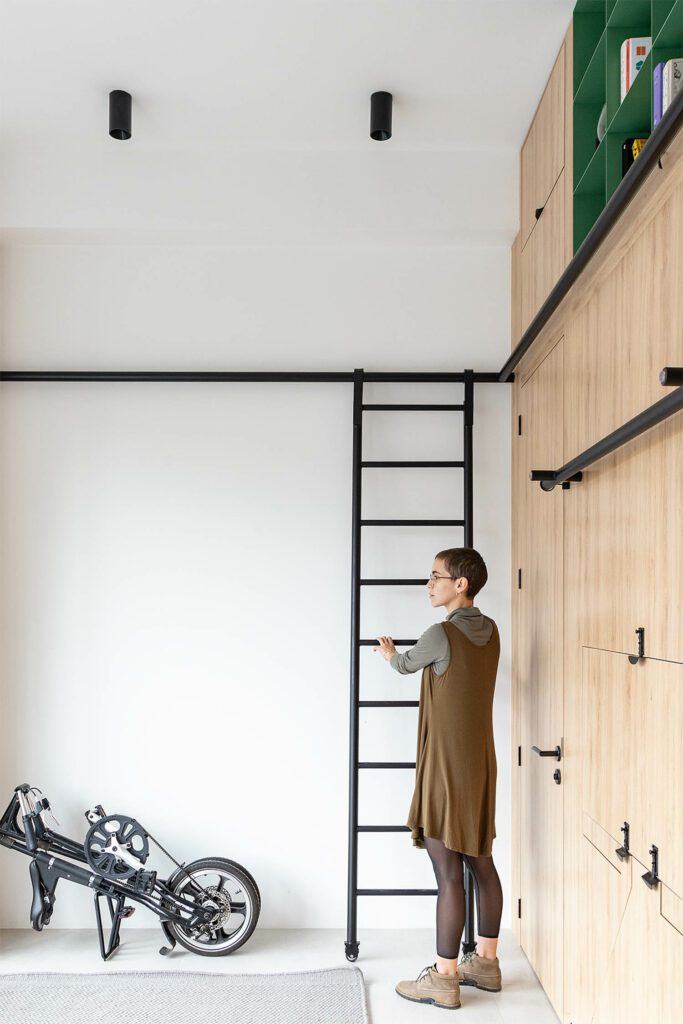 A matte-lacquered tubular metal ladder, on rails and casters, creates access to overhead storage.