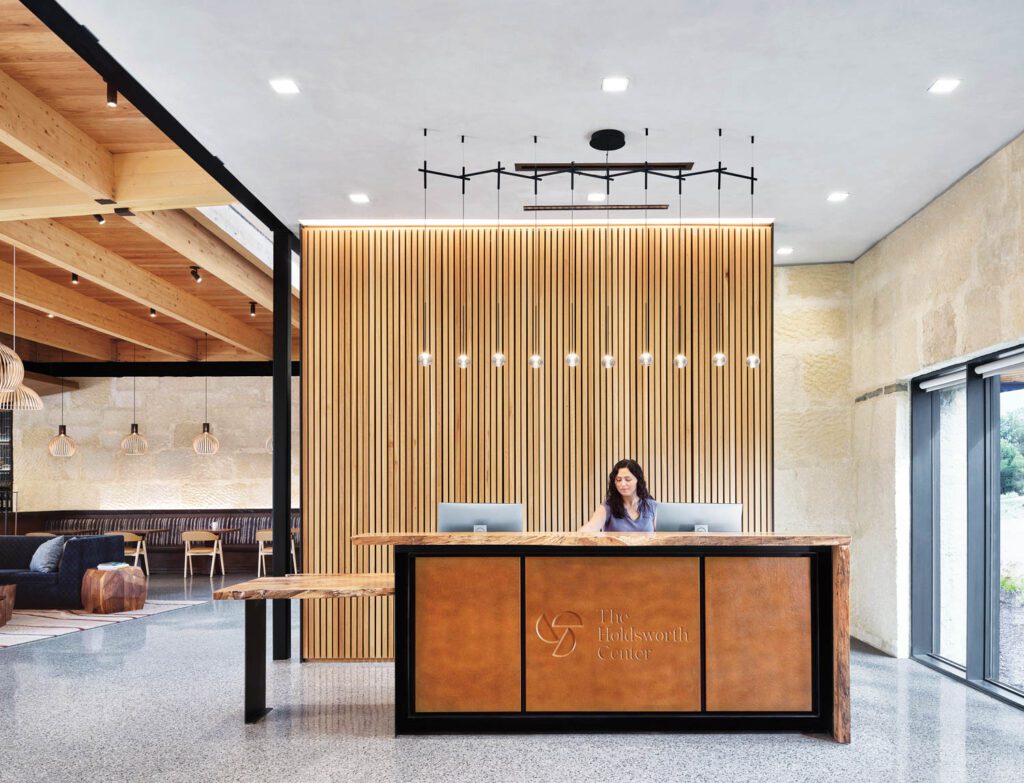 Main reception has a custom desk of live-edge pecan and blackened steel with leather inserts backed by a hemlock-slat partition.