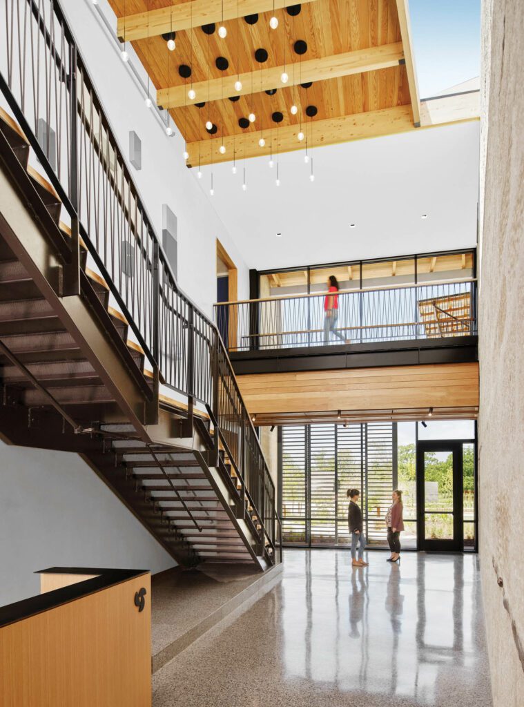 The building’s atrium features a massive wall of locally sourced limestone topped by a skylight opposite a staircase in painted steel and Douglas fir. 