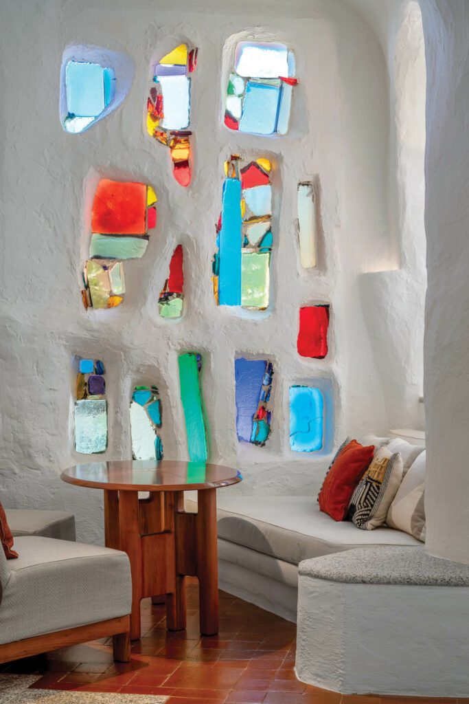 The stained glass embedded in the wall reflects in the glazed top of a lava-stone cocktail table
