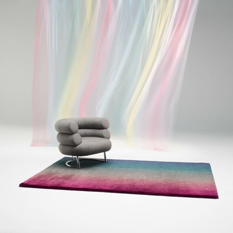 A pastel curtain flows over a chair atop a Field rug by Peter Saville for Kvadrat